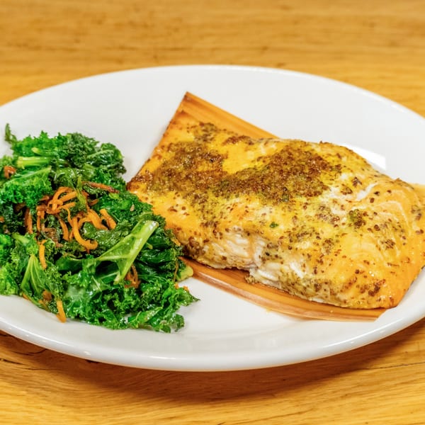 Cedar plank salmon with a mustard glaze, served alongside a vibrant green kale salad.